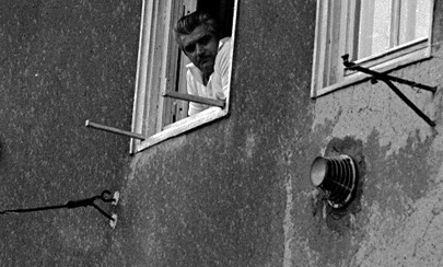 Bewohner schaut aus dem Fenster eines heruntergekommenen Hauses